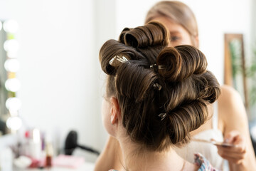 Fototapeta premium The hairdresser curls the model's hair. Curling iron for curling hair close-up.