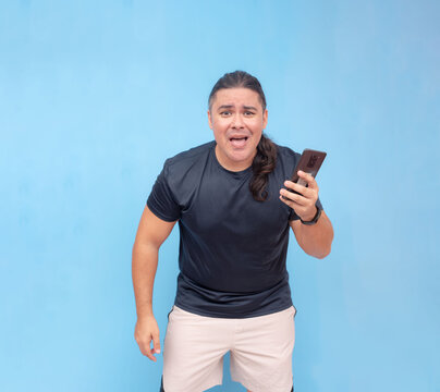 An uneasy biracial man holding a smart phone in one hand while leaning forward. Isolated on a blue background.