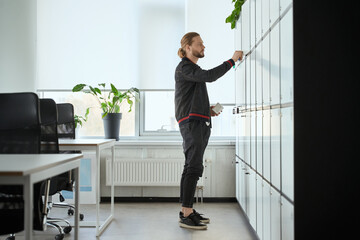 Bearded man closes the door of locker in coworking space