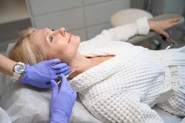 Smiling adult lady getting neck injection in beauty salon