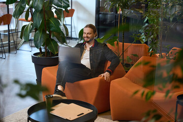Smiling male comfortably settled down with laptop in lounge area