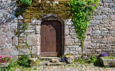 Fototapeta na wymiar Wooden door in a stony wall in the old center of the village Locronan in Brittany with historic stone houses, France