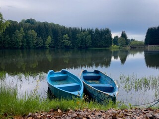 Two blue wooden boat on a lake surrounded by coniferous trees
