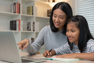 Mother teaching lesson for daughter by laptop. Asian young little girl learn at home. Do homework with kind mother help, encourage for exam. Asia girl happy Homeschool. Mom advise education together.