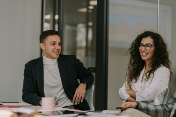 A young handsome male person listening to his female colleague having fun conversation with the colleague at the other side of the table