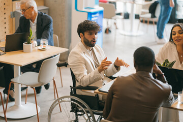 Good looking handicapped businessman in wheelchair having meeting with his partners. They are discussing project details