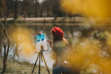 Woman wearing red hat is painting on an easel