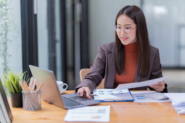 Smiling young Asian businesswoman sitting  with laptop computer on desk in the office.