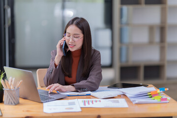 Sharing good business news. Attractive young businesswoman talking on the mobile phone and smiling while sitting at her working place in office and looking at laptop PC.