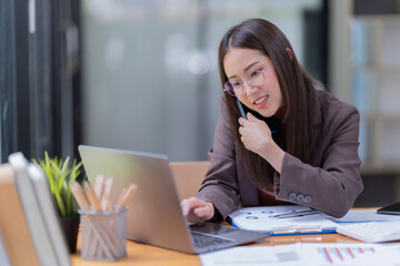 Smiling young Asian businesswoman sitting  with laptop computer on desk in the office.