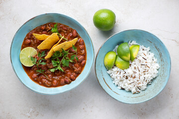 Turquoise bowls with chili con carne, mixed rice and nachos. Flat lay on a light-beige stone background, horizontal shot