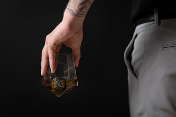 Man in blakc shirt holding whisky glass woth whisky stones after a long day, with sleeve rolled up.