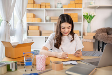 Obraz na płótnie Canvas Woman Writing Customer Details for Shipping in Home Office, Packing Box and Writing Customer Information for Efficient Shipping, E-Commerce and Online Selling Concept.