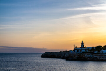 Landscape view of Cala Santandria with lighthouse at sunset Menorca, Spain.
