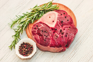 Fresh piece of meat large beef steak on the bone ossobuco with pepper, rosemary on the board.