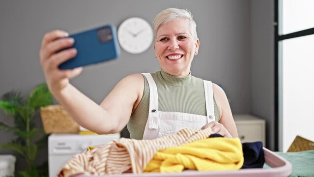 Middle age grey-haired woman smiling confident make selfie by smartphone at laundry room