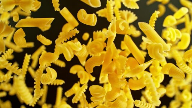 Super slow motion of flying uncooked Italian pasta mix on black background. Filmed on high speed cinema camera, 1000 fps, placed on high speed cine bot, following the object. Speed ramp effect.