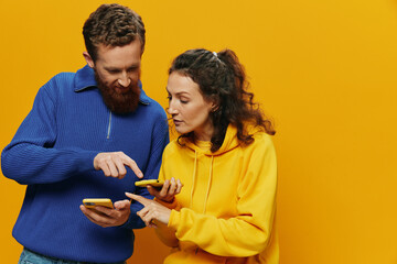 Woman man cheerful couple with phones in hand social networking and communication crooked smile fun and fight, in yellow background. The concept of real family relationships, freelancers, work online.