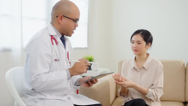 Beautiful asian women patient hurt hand consulting with Handsome asian professional doctor about pain in her hand feeling suffering and The doctor writing and analyzing her symptoms on the tablet.