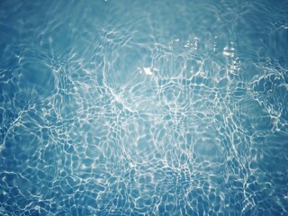 Blue water with ripples on the surface. Defocus blurred transparent blue colored clear calm water surface texture with splashes and bubbles. Water waves with shining pattern texture background.