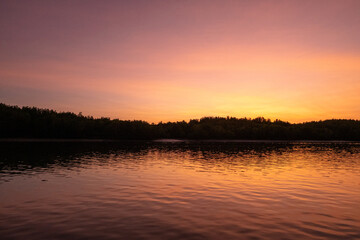 Fototapeta premium Colorful sky and the sea during the sunrise, with silhouette of the forest on the background