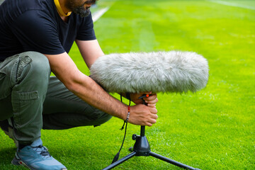 A sound technician is placing a shotgun microphone at the edge of the football field.