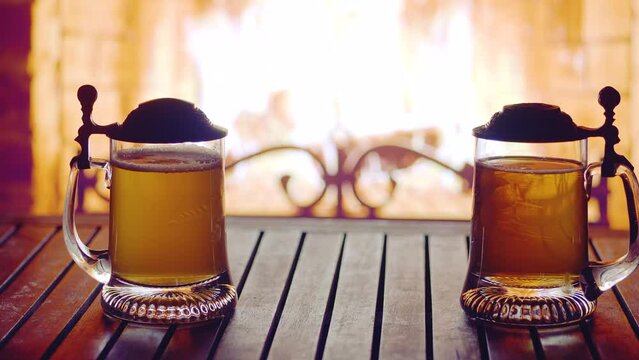 Image of alcohol.Two mugs of beer on the table near the fireplace. Cozy mood.