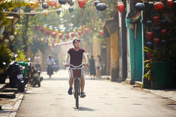 Tourist riding bicycle in old town. Street of ancient city decorated with traditional lanterns, Hoi...