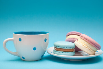 Macaroons and cup of tea or coffee on blue color background, dessert and sweet food
