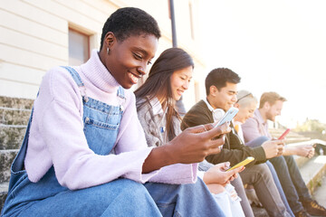 Technology Addicted smiling group of cheerful students using mobiles. They check multimedia in...