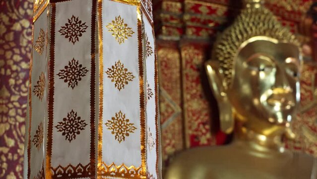 Decorative fabrics hang from the ceiling of a Buddhist temple with a gilded Buddha statue, Thailand
