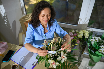Close-up beautiful inspired woman, florist, event manager putting a greeting card in a floral...