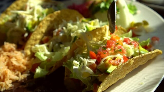 Spoon adding salsa to hard shell corn taco pork cheese and lettuce Mexican delicious food