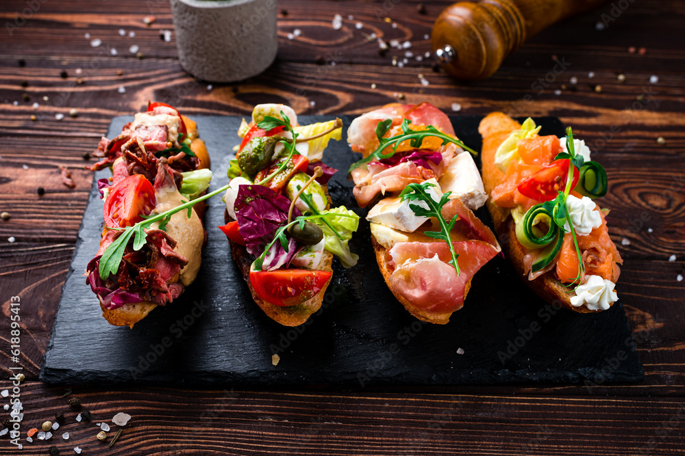 Wall mural Appetizers bruschettas with beef slices, capers, cherry tomatoes, mozzarella, salmon, cucumber, lettuce.