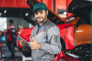 Portrait happy automobile mechanic man looking at camera holding digital tablet and showing thumbs up. Diagnostic and repairing vehicle at garage automotive.