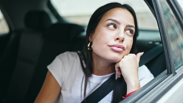 Young beautiful hispanic woman passenger sitting on car with relaxed expression at street