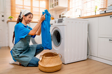 Asian housekeeper or housemaid hold and check blue cloth before put into washing machine during home service to customer.
