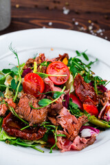 Green salad with cherry tomatoes, beef, cucumbers, sun-dried tomatoes, lettuce, arugula and green peas, lunch.