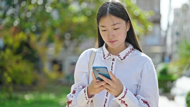 Young chinese woman using smartphone smiling at park