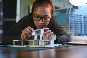 Architecture students diligently make house model building samples with paper architecture and tools at night in their alone room.