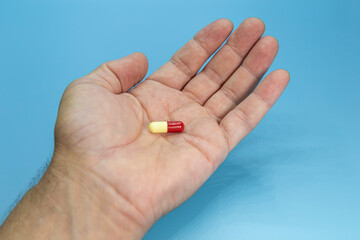 Man's hand holding a red and yellow pill on a blue background