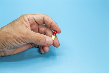 A hand holds a red-yellow pill on a blue background. Focus on the pill.