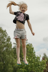 A child jumps on a trampoline. The girl jumped in the air. A child with positive emotions jumps....