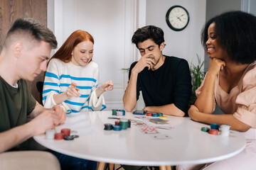Portrait of happy diverse friends having home fun party on weekends playing poker game sitting at...