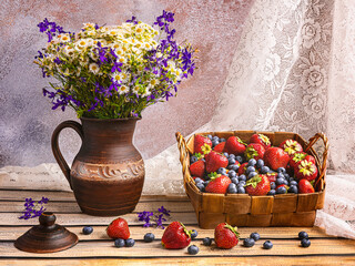 Basket of fresh harvest of strawberries and blueberries, vintage ceramic vase with wildflowers. Summer still life