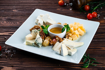 Set for wine dorblu cheese, parmesan, brie white cheese, walnuts, grapes, honey and mint on a wooden table.