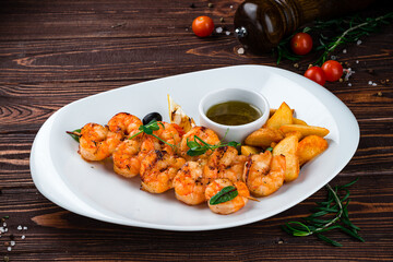 Fried shrimp on a skewer with rustic potatoes, lemon, tomatoes, olives and sauce, fresh lunch.