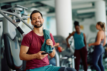 Happy athletic man using mobile phone while working out in gym and looking at camera.