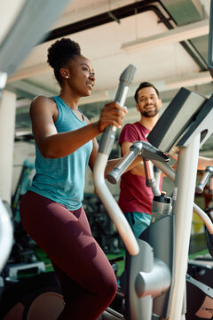 Black female athlete working out on cross trainer in health club.