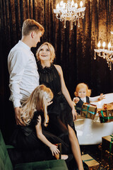 Merry Christmas and Happy Holidays! Cheerful and happy family with Christmas presents in golden wrappings and dark background. Children are having fun. Loving family with gifts in the room.